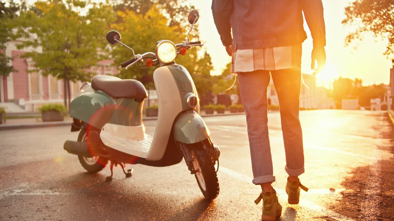 여름에 해가 뜨는 동안 그의 초록색 모페드에 걸어서, 그 위에 앉아서 길거리에서 운전하는 젠 옷을 입은 남자의 클로즈업. 헬을 입은 곱슬머리 남자는 여름에 빛 날씨에 모페드에서 앉아 있습니다.