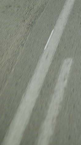 eine bewegungsunklare sicht auf eine asphaltierte straße mit sichtbaren weißen fahrbahnmarkierungen, leichte reflexion von einem nahe gelegenen objekt auf der seite