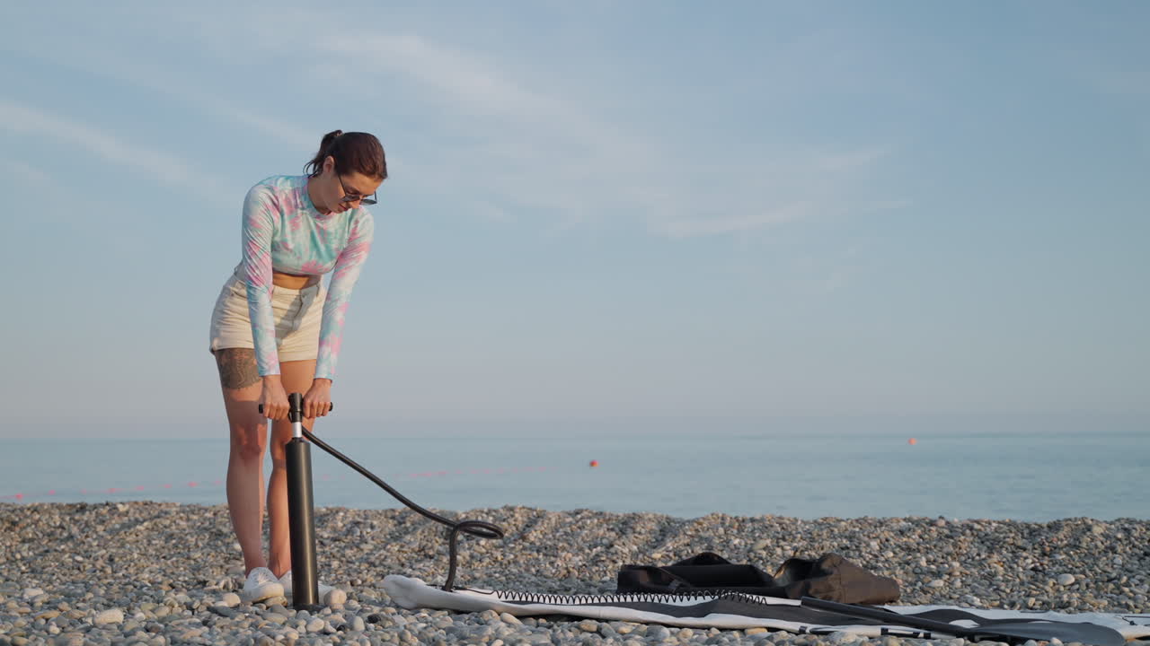 mujer preparando una tabla de remo inflable en una playa de guijarros