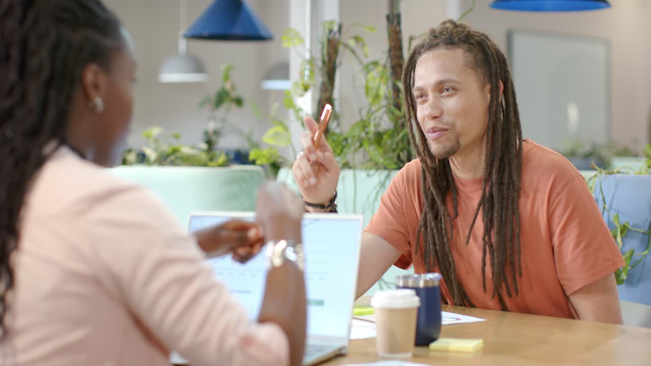 Afroamerikanske kolleger diskuterer på kontoret, kvinne starter demonstrasjon på bærbar PC, mann lener seg med penn