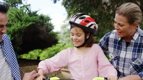 Girl-sitting-on-a-bike-while-happy-parents-giving-high-five-and-hugging-her