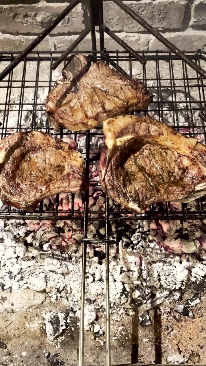 Verticale. Bistecche di manzo T-bone grigliate su griglia metallica su braci di legno ardenti