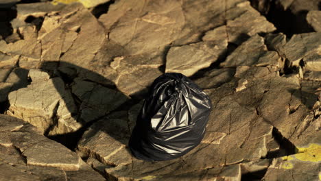 una bolsa de basura negra en una playa rocosa