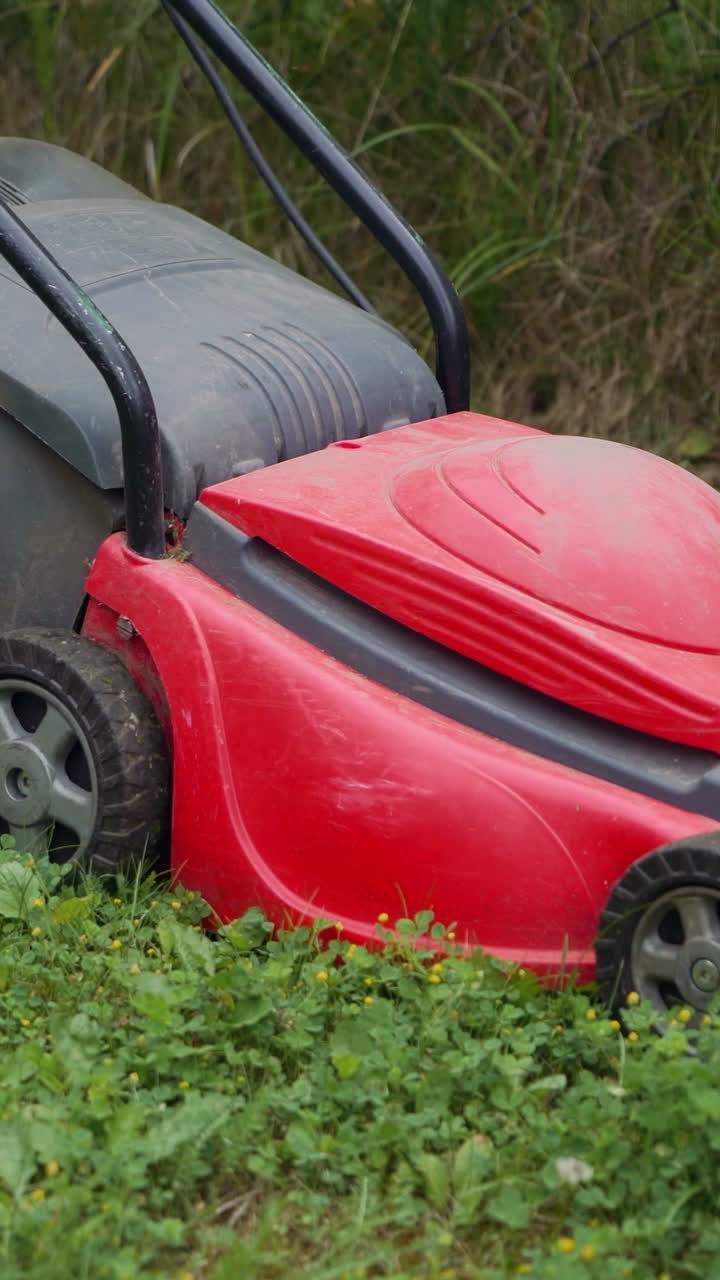 girl is mowing weeds by lawn mower in the garden near the fence in the summer Vertical video