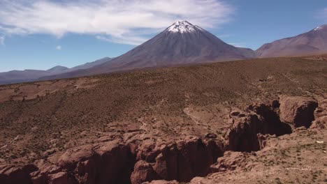 aerial view of snow-capped licancabur volcano near san pedro de atacama. a dry canyon cuts through the desert in the foreground, adding depth to the high-altitude landscape.