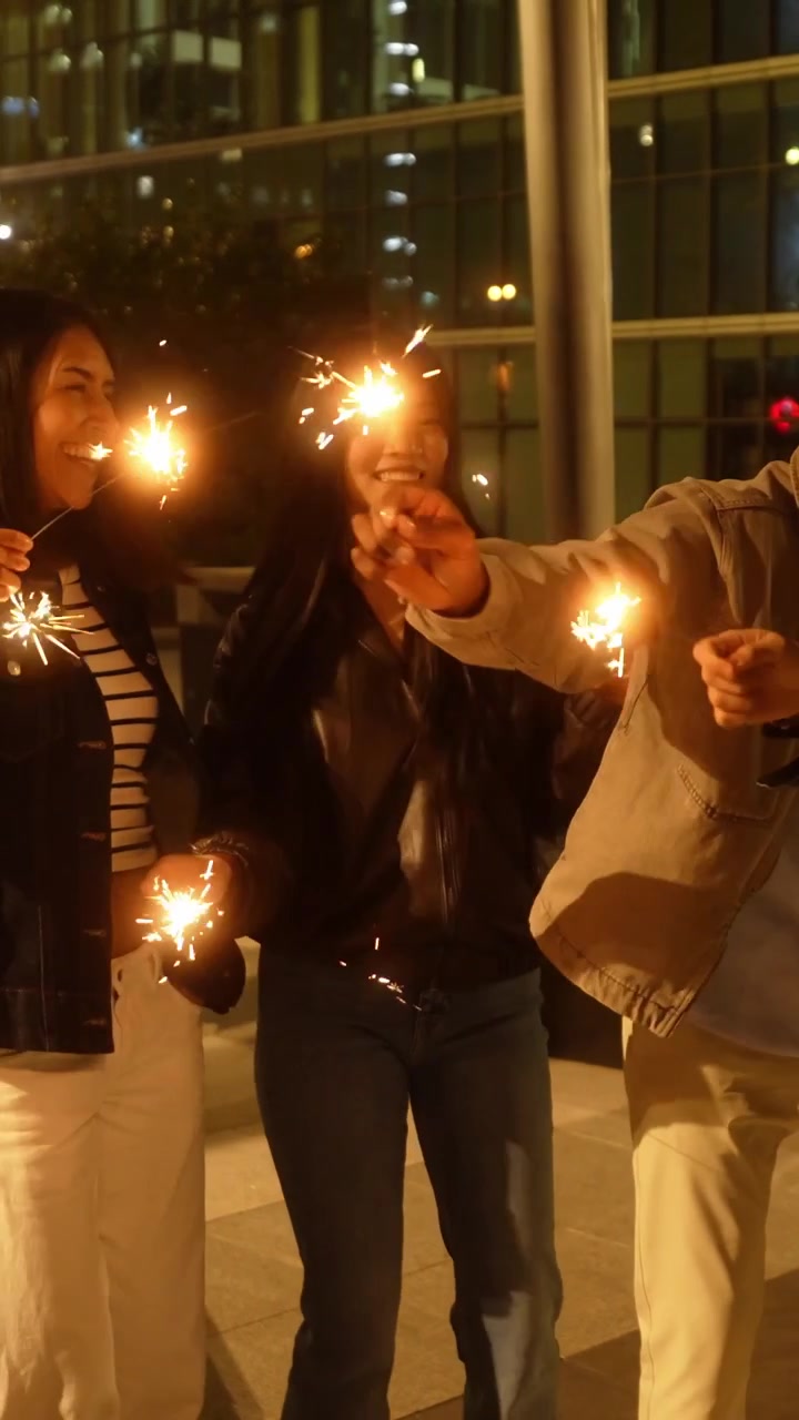 Jóvenes amigos felices celebrando con bengalas de noche en la ciudad