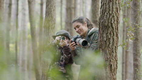 白人の女性と少年が森の木々の間に立ち、単眼で野生生物を観察し、プロのカメラで写真を撮る