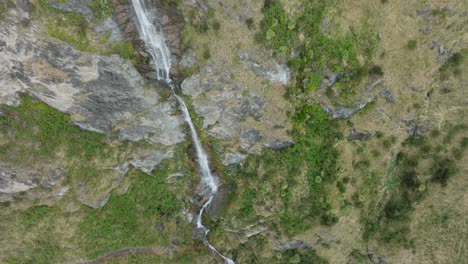 Top-down-rotating-aerial-view-of-scenic-picturesque-waterfall-winding-through-rugged,-rocky-landscape-in-the-remote-wilderness-of-New-Zealand-Aotearoa