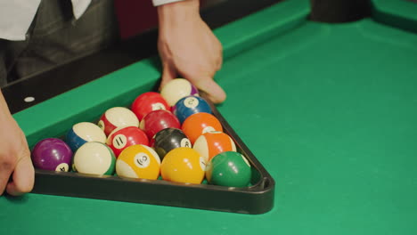 close up of player in white shirt aiming at well-arranged colorful billiard balls in triangle formation on green pool table. blurred foreground emphasizes intense focus