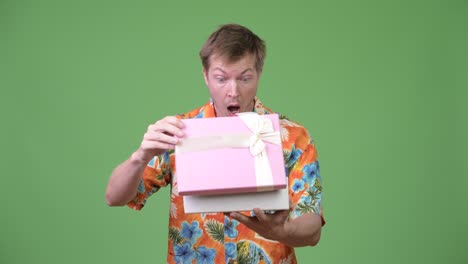 young handsome tourist man opening gift box and looking surprised