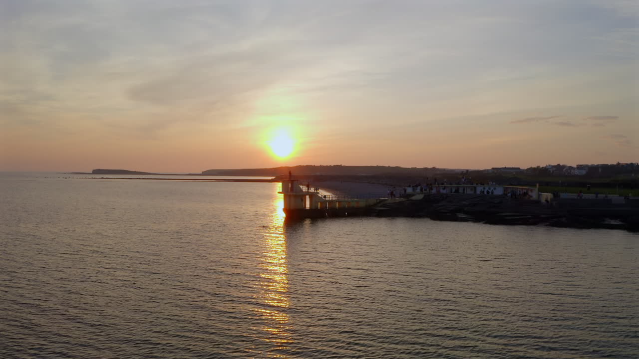 Sunset glow surrounds diving platform as waves shimmer with golden light, aerial tracking right