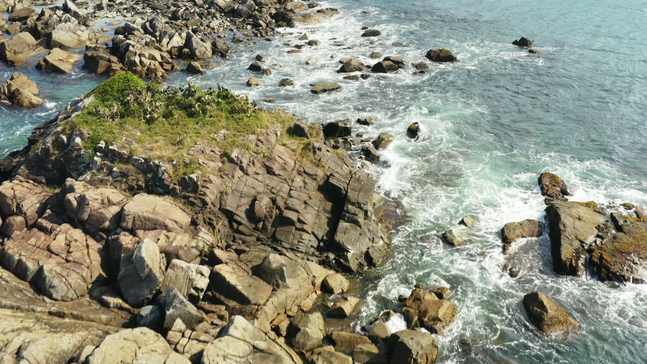 Dalgaların kıyı kayalarına çarptığı havadan sinematik görünüm, Praia Armacao, Florianopolis, Santa Catarina, Brezilya.