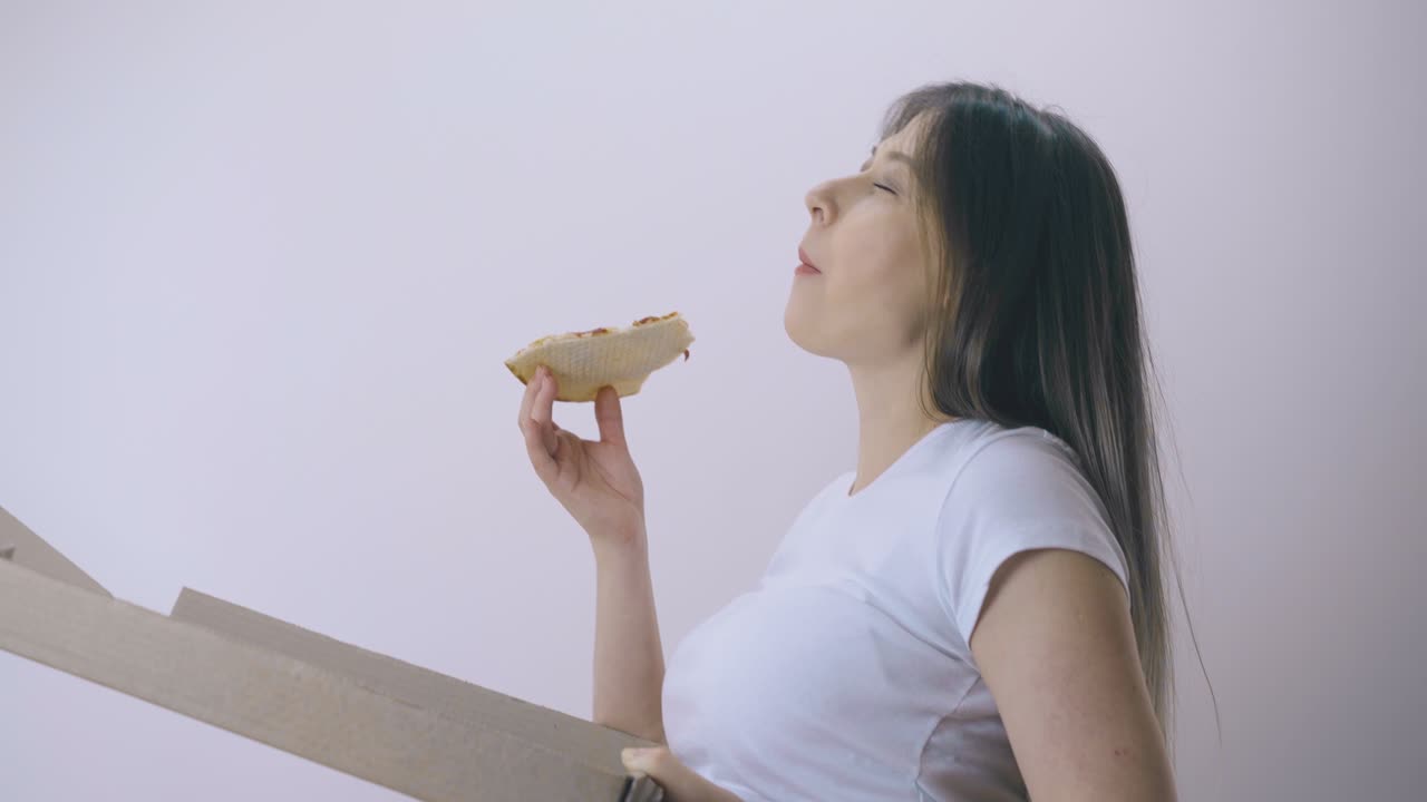 임신한 여자가 빛의 벽에 있는 상자에서 맛있는 피자를 먹습니다.