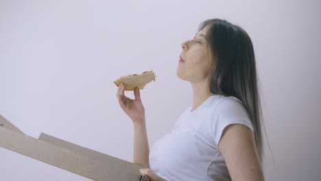 pregnant lady eats delicious pizza from box at light wall