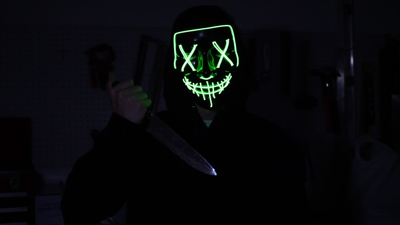 un aterrador asesino slasher con una máscara de terror de halloween tirando un cuchillo a su víctima de asesinato en la oscuridad