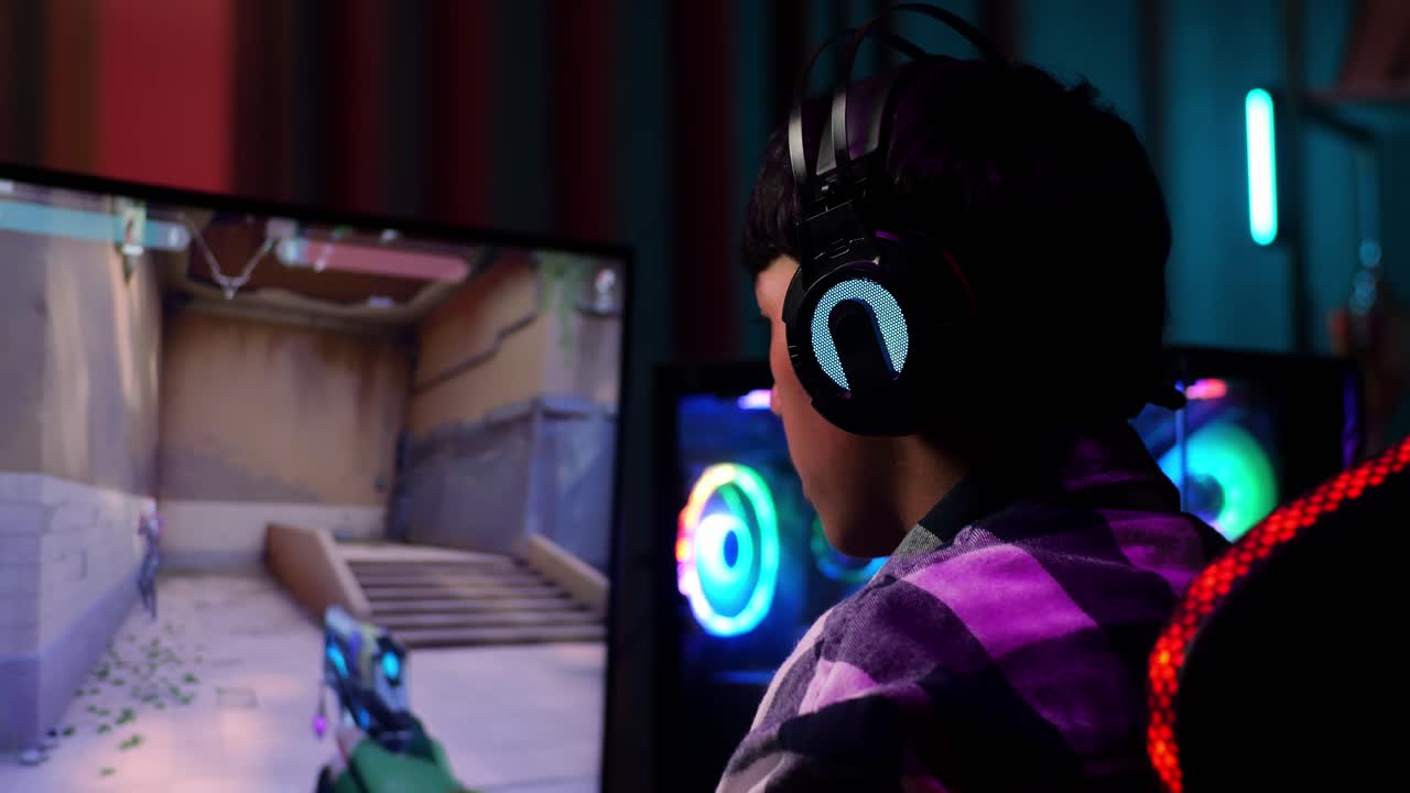 Primo piano di un giovane gamer asiatico entusiasta che festeggia la vittoria e balla mentre gioca a un videogioco sparatutto online al computer.