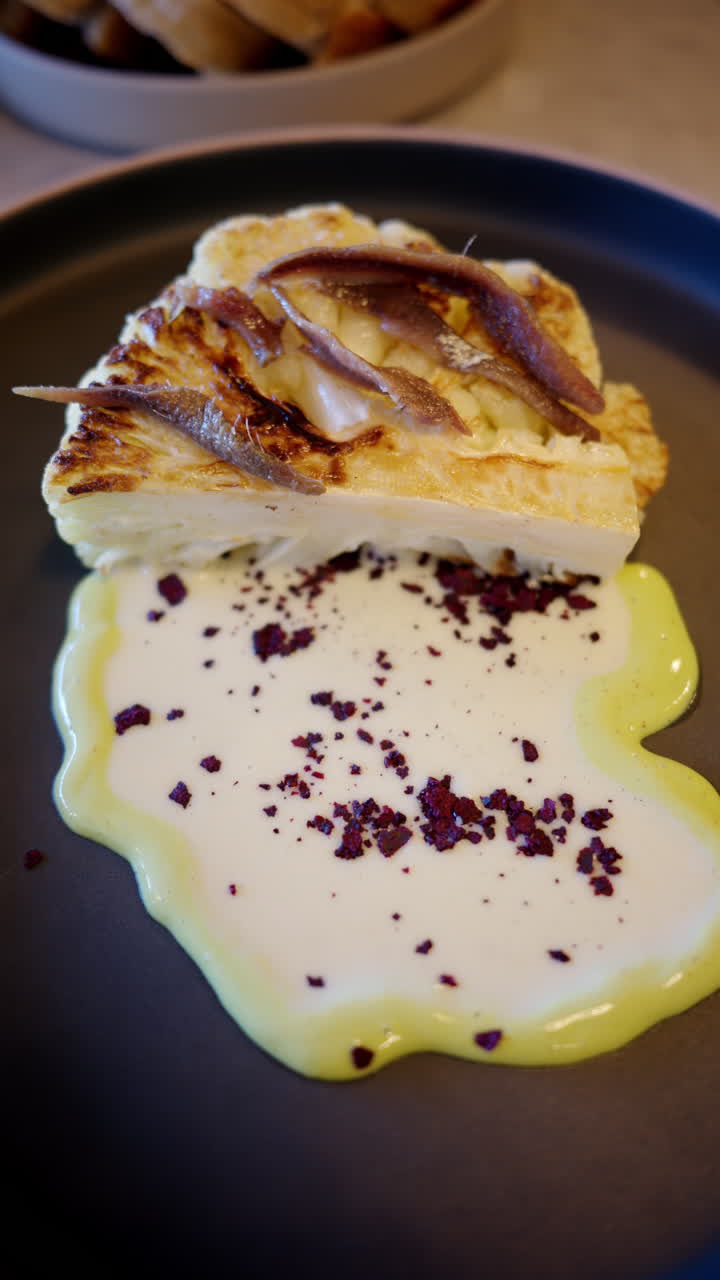 Cauliflower steak with a white sauce on a black plate. Vertical