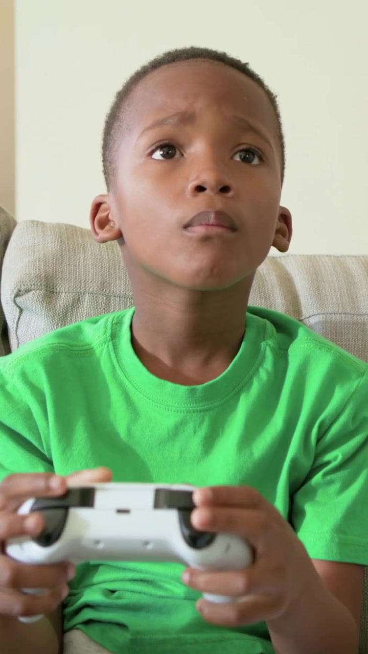 Vertical video: Pressing white controller, boy wearing green tee playing game at home for fun