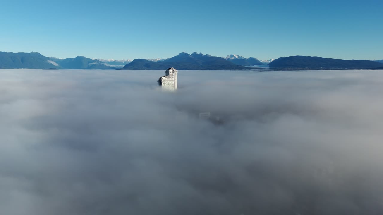 Langley, Canada - A Tall Building Rises Above a Thick Blanket of Fog with Mountains Visible in the Distance - Aerial Drone Shot
