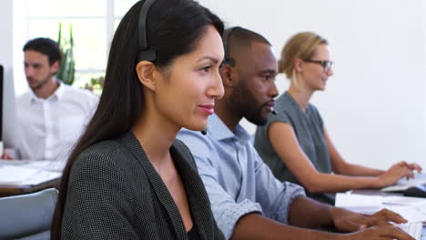 Asian-woman-in-headset-smiles-to-camera-in-open-plan-office