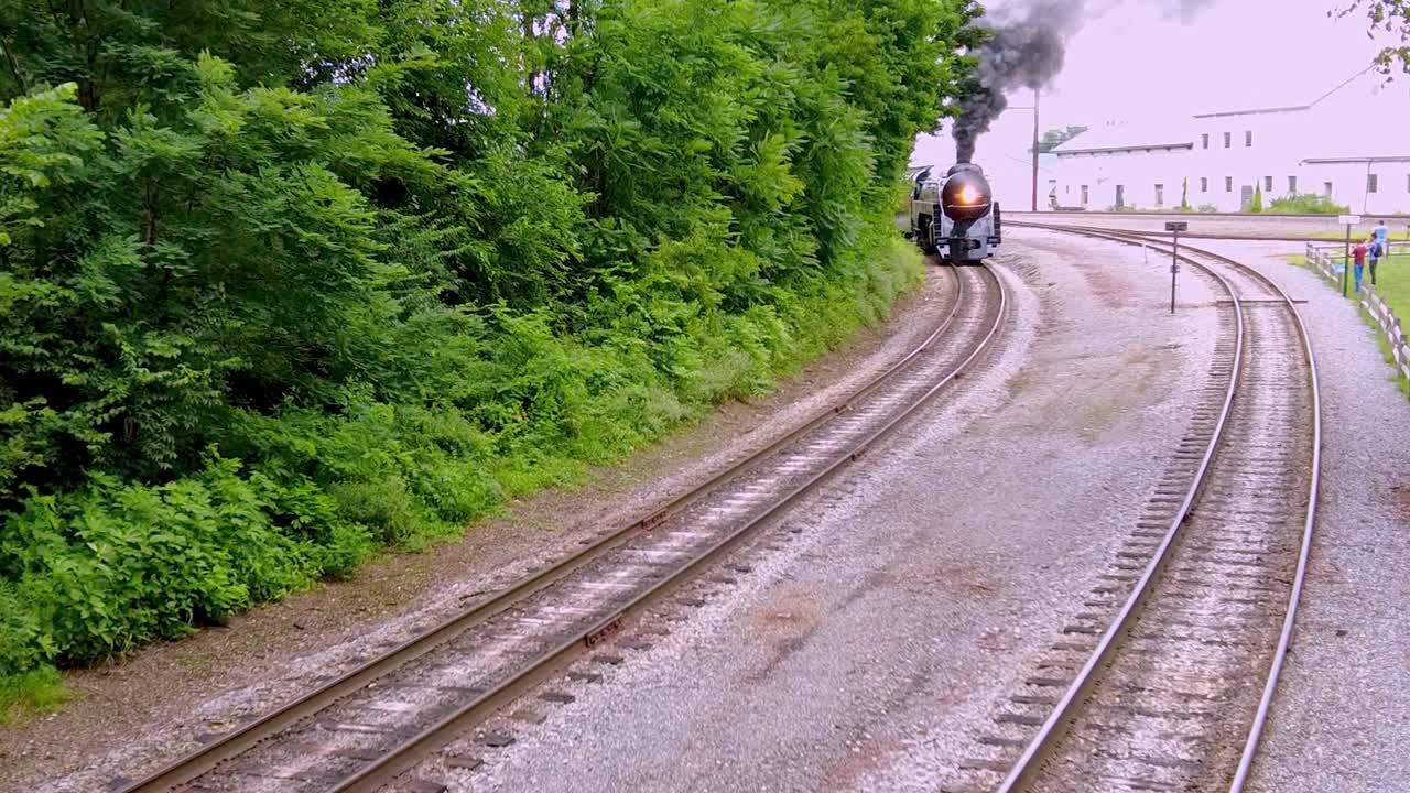 una vista elevada de un gran tren de pasajeros con motor de vapor que sopla humo negro que pasa por una vía muerta en un día nublado