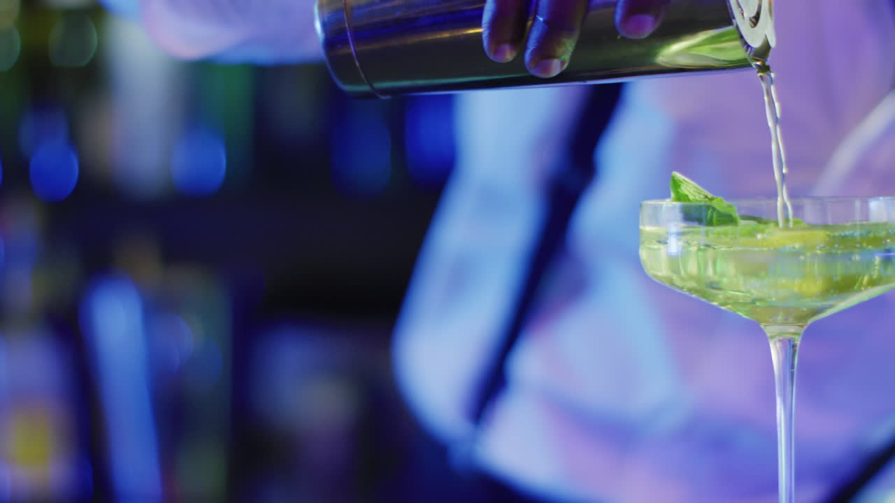 Video del busto di un barman afroamericano che prepara un cocktail verde al bar.