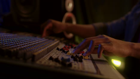 cierre de las manos masculinas trabajando en la placa de sonido o mezclador en el estudio oscuro mientras el hombre domina una canción