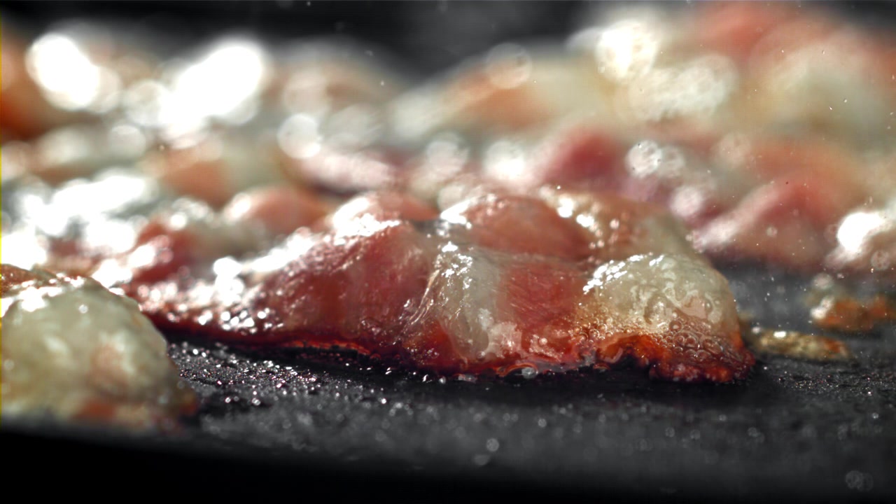 Primo piano di pancetta che sfrigola e frigge su una padella calda