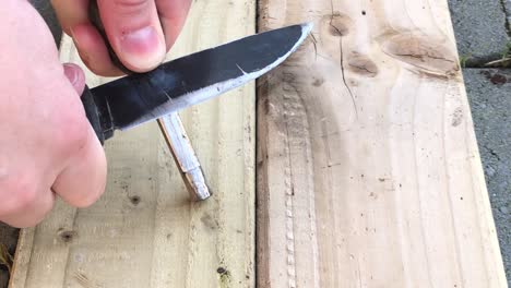 vista de cerca de la mano de la persona haciendo chispas usando un cuchillo y acero en una tabla de madera