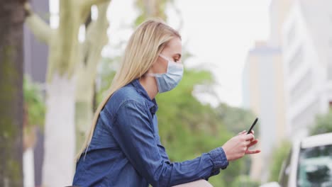 Side-view-of-Caucasian-woman-wearing-a-coronavirus-Covid19-mask-and-using-her-phone