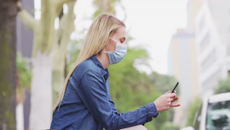 vista lateral de una mujer caucásica con una máscara de coronavirus covid19 y usando su teléfono