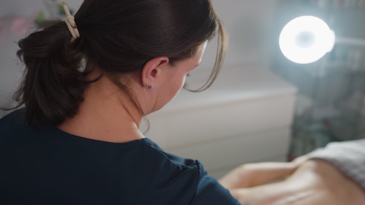 Over shoulder view of treatment provider working on customer body in modern spa room under bright professional light capturing focused technique and serene atmosphere for wellness session