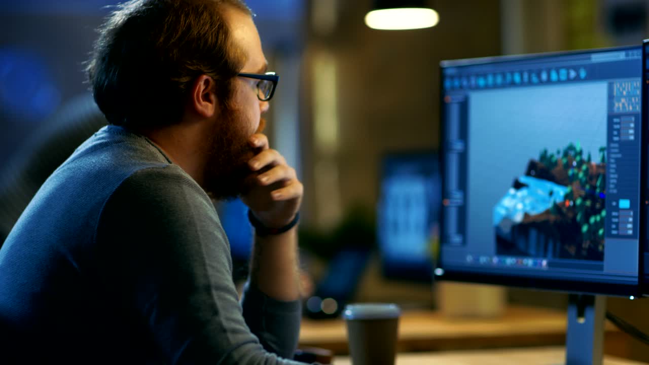 el desarrollador de juegos masculino trabaja en un nuevo diseño de nivel. es un hombre guapo y barbudo con gafas y trabaja en una oficina creativa con otras personas talentosas.