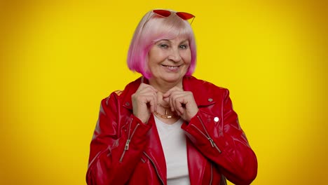 una mujer mayor elegante con cabello rosa y una chaqueta de cuero roja sonríe con confianza a la cámara.