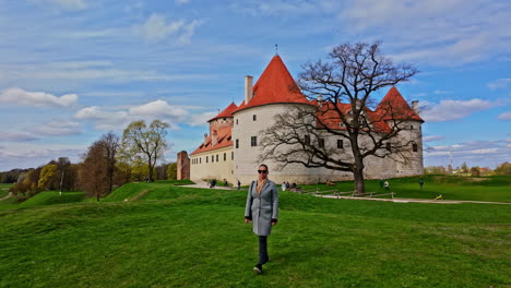 Mujer-Solitaria-Caminando-Sobre-El-Césped-Frente-Al-Histórico-Museo-Del-Castillo-De-Bauska,-Letonia