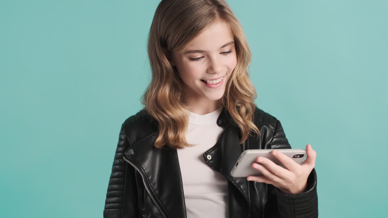 Teenage Caucasian girl in leather jacket watching videos on her smartphone.