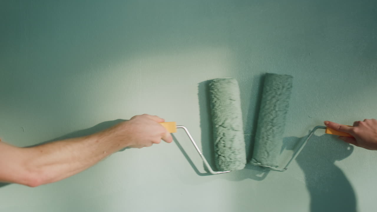 Unknown couple doing decoration work in home. People pushing rollers on wall.