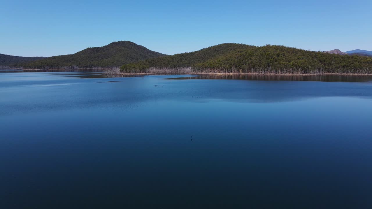 어드밴스타운 호수의 잔잔한 물에 반사되는 푸른 하늘 - 힌즈 댐에서 숲이 우거진 산 - 골드 코스트, 퀸즐랜드, 호주