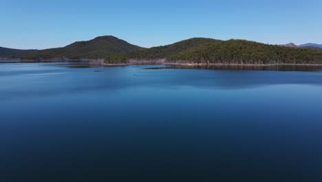 blue sky reflecting at the still water of advancetown lake - forested mountain from hinze dam - gold coast, queensland, australia