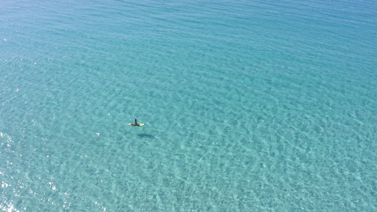 Stand up paddle boarder floating across crystal clear water in Son Bou along Menorca's spectacular coastline in Spain