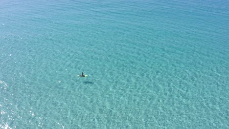 Stand-up-paddle-boarder-floating-across-crystal-clear-water-in-Son-Bou-along-Menorca's-spectacular-coastline-in-Spain