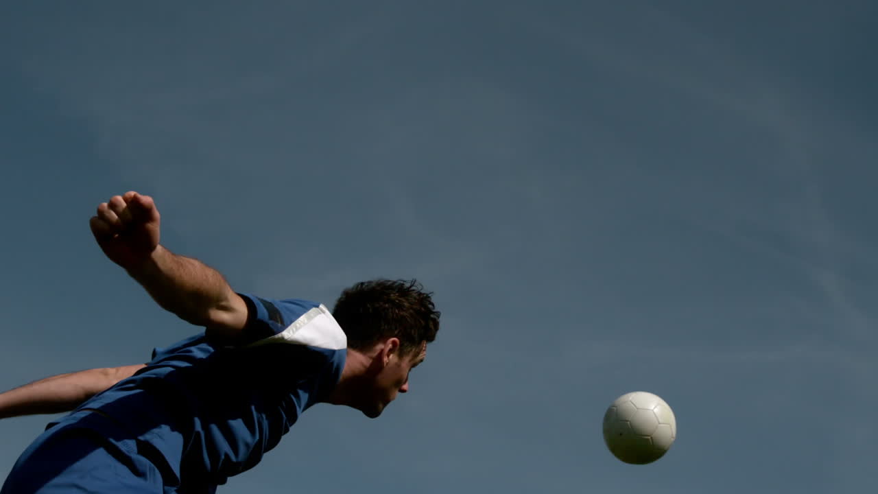 Football player heading the ball under blue sky