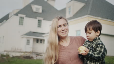 Portrait-of-a-happy-mother-with-a-baby-in-her-arms-against-the-background-of-a-large-house