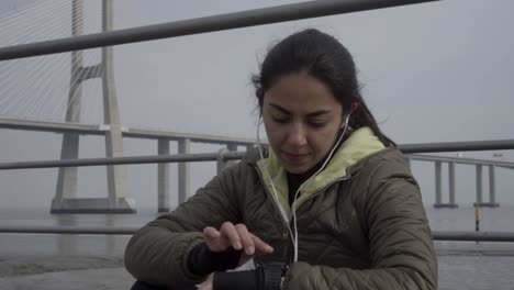 mujer joven pensativa poniendo el reloj deportivo antes del entrenamiento