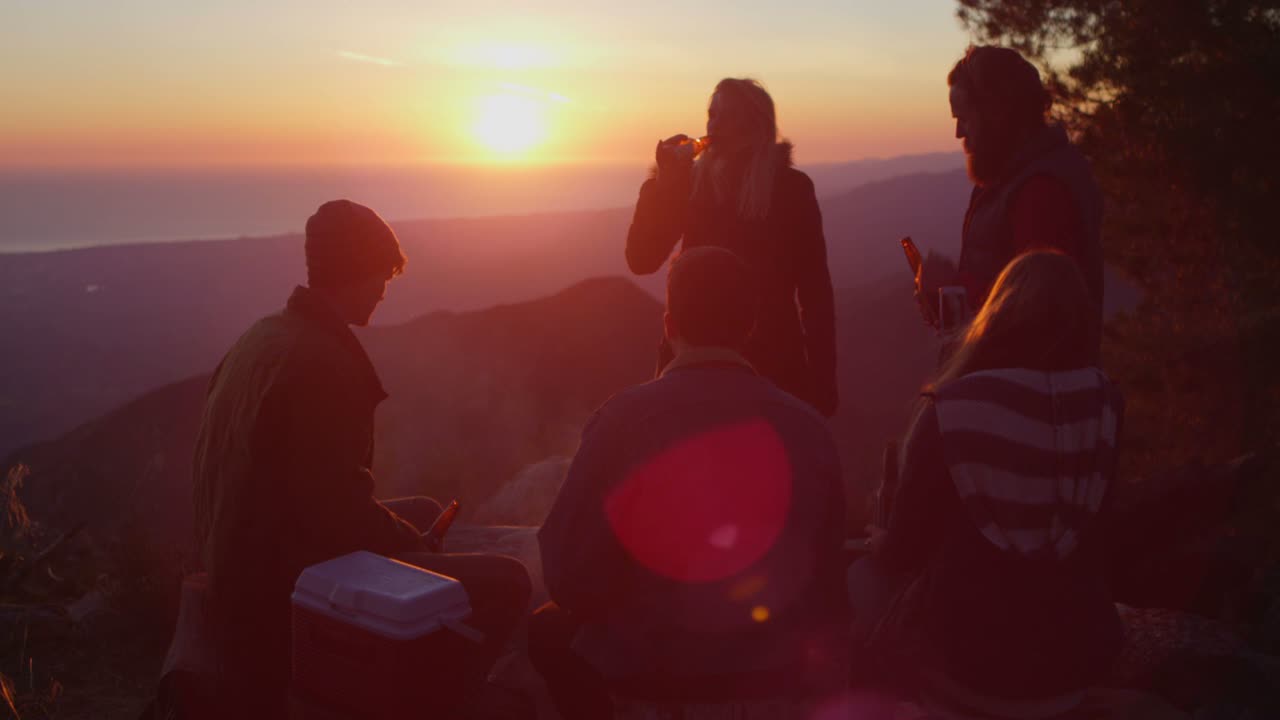 A group of friends drink beer at a campsite as the sun sets