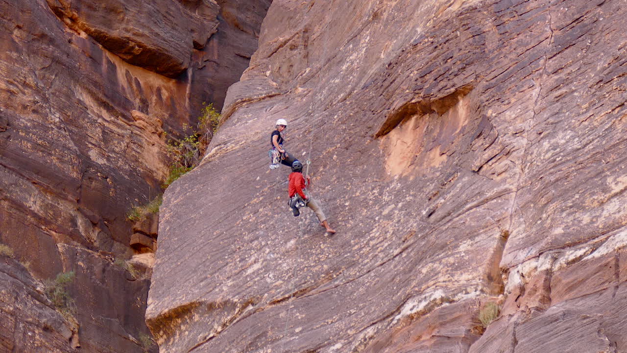 Man and woman repel down a massive rock face in Zion National Park, Utah