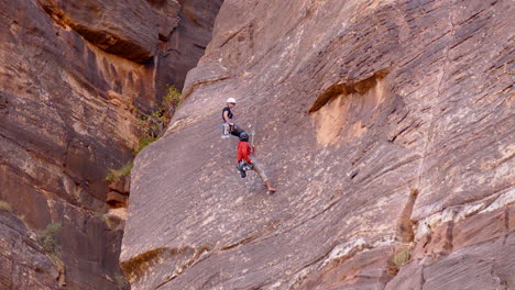 man and woman repel down a massive rock face in zion national park, utah