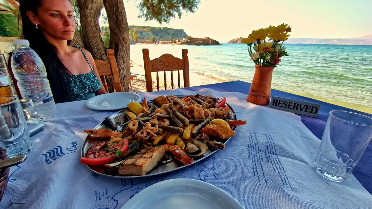 Woman sitting at a seaside restaurant table with a plate full of seafood