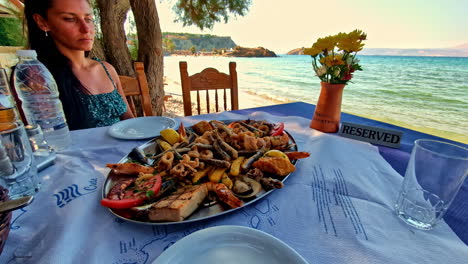 woman sitting at a seaside restaurant table with a plate full of seafood