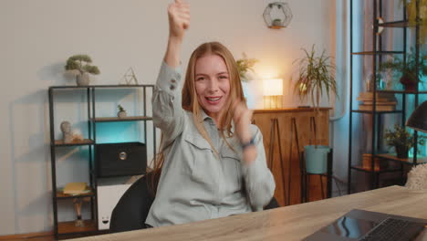 happy caucasian woman looking at camera shocked by sudden victory sitting at home office table